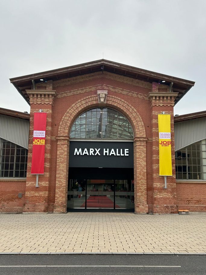 Eingang der Marx Halle mit roter Backsteinfassade und bunten Bannern.